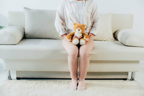 colpo ritagliato se giovane donna seduta sul divano a casa e tenendo orsacchiotto
 - Foto, immagini