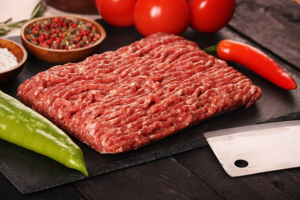surové mleté maso na plech, přísady pro burger s rajčaty, pepřem, cibulí, kořením a kořenem na černém pozadí. - Fotografie, Obrázek