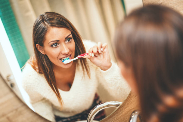jeune femme brossant les dents devant le miroir de salle de bain
 - Photo, image