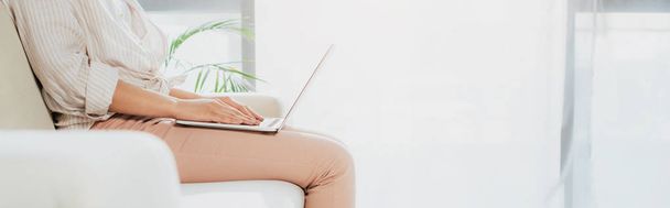 панорамный снимок женщины с ноутбука, сидящей дома на диване
 - Фото, изображение