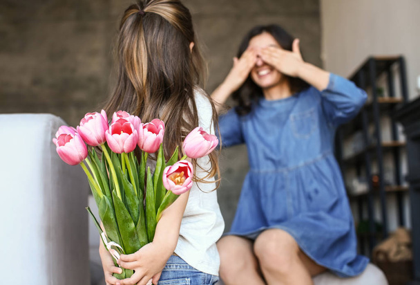 Μικρό κορίτσι κρατώντας μπουκέτο λουλουδιών για τη μητέρα πίσω από την πλάτη της στο σπίτι - Φωτογραφία, εικόνα