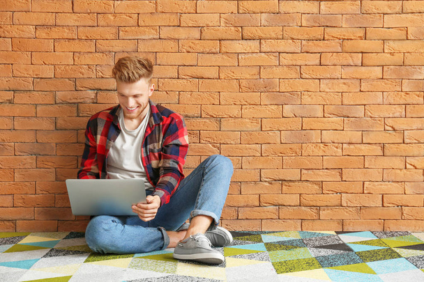 Beau jeune homme avec ordinateur portable assis près du mur de briques
 - Photo, image