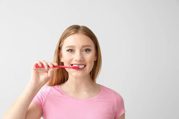 Piękna kobieta czyszczenia zębów na jasnym tle - Zdjęcie, obraz
