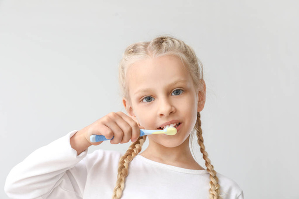Little girl cleaning teeth on light background - Foto, imagen
