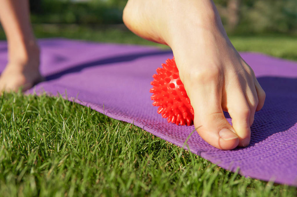 Woman massage feet with spiny plastic red massage ball  in summer park.  Self myofascial release  concept, love your feet - Photo, Image