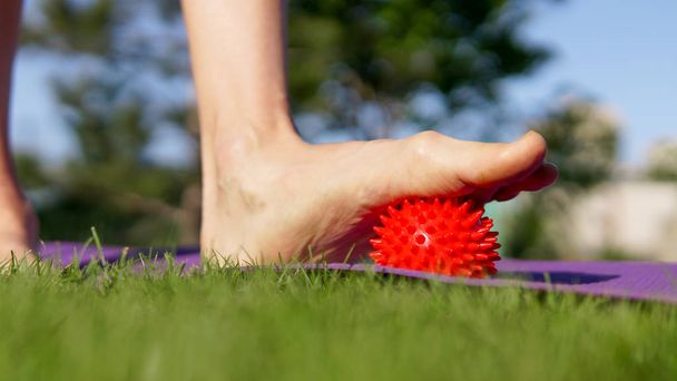 夏の公園でスパイシーなプラスチック製の赤いマッサージボールを持つ女性のマッサージ足。自己神秘的な解放の概念は、あなたの足を愛し - 写真・画像