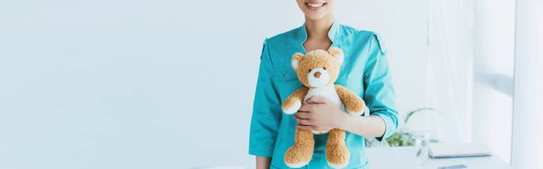 panoramic shot of smiling latin doctor holding teddy bear - Photo, Image