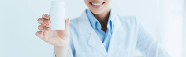 panoramic shot of smiling latin doctor showing container with pills - Foto, Imagem