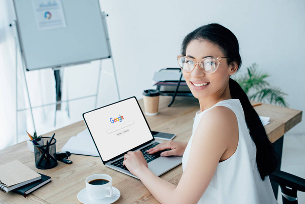 KYIV, UKRAINE - APRIL 26, 2019: Smiling businesswoman looking at camera while using laptop with Google website on screen.  - 写真・画像