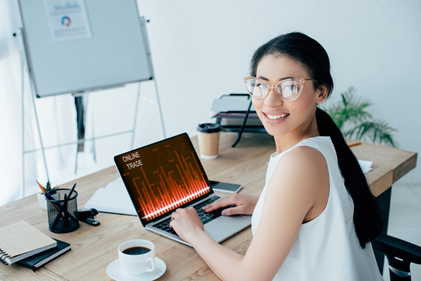 młoda latynoska bizneswoman uśmiechnięta do kamery podczas korzystania z laptopa ze strony internetowej handlu online na ekranie - Zdjęcie, obraz