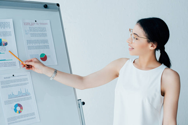 pretty businesswoman pointing with pencil at flipchart with infographics - Φωτογραφία, εικόνα
