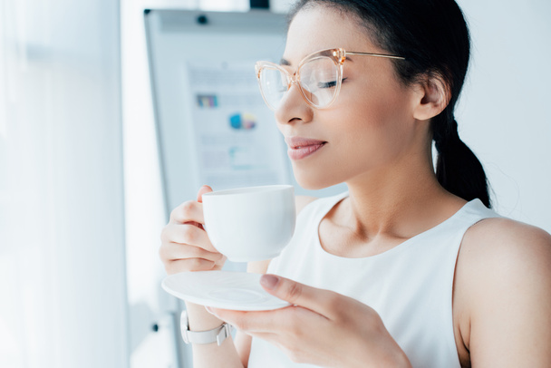 beautiful businesswoman enjoying coffee flavor while holding coffee cup with closed eyes - Photo, Image