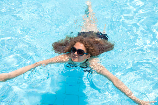 A young girl swims in the pool on a summer day outside - Photo, image
