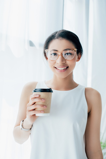 χαρούμενη Λατινική επιχειρηματίας που χαμογελά στην κάμερα ενώ κρατά καφέ για να πάει - Φωτογραφία, εικόνα