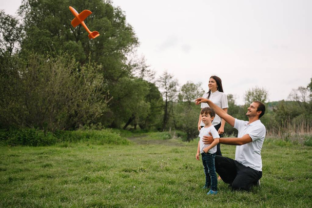 Ojciec, matka i syn bawią się zabawkowym samolotem w parku. przyjazna rodzina. Ludzie bawią się na świeżym powietrzu. Obraz wykonany na tle parku i błękitnego nieba. koncepcja szczęśliwej rodziny. - Zdjęcie, obraz