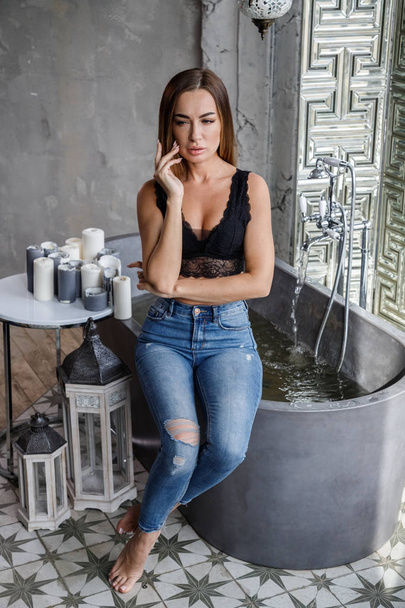 Closeup portrait of beauty young woman in black lingerie and blue jeans posing at modern bathroom interior - Zdjęcie, obraz