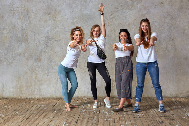 group of young girls are posing against the wall smiling and showing gestures with their hands. Gray background, save space. - Fotografie, Obrázek