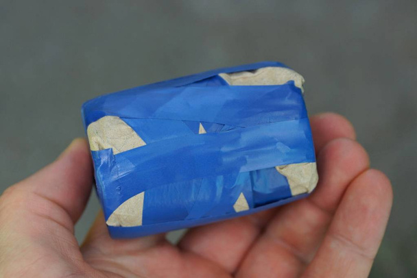 Finger halten Box mit blauem Klebeband auf grauem Hintergrund umwickelt - Foto, Bild