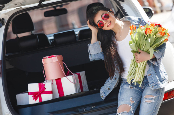 Молодая привлекательная женщина с подарками. Девушка в машине. Стильная дама под открытым небом
. - Фото, изображение