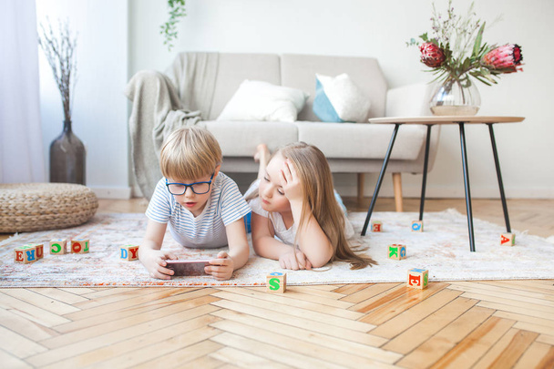 zwei Kinder spielen Smartphone. Jungen und Mädchen zu Hause, die am Handy zuschauen. digitale Kinder im Haus. - Foto, Bild