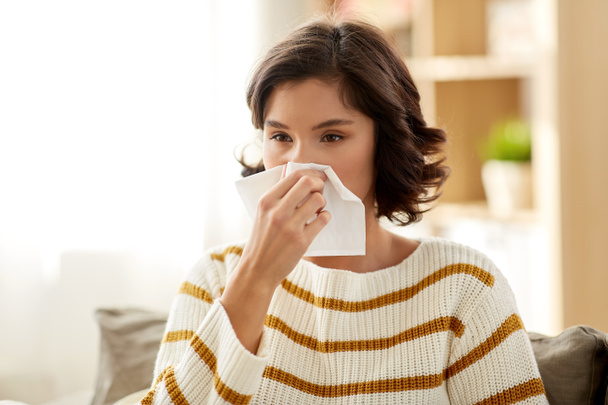 sick woman blowing nose in paper tissue at home - Foto, Imagen