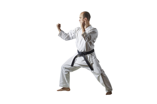 Na bílém izolovaném pozadí sportovec s černým pásovým vlakem trénuje formální cvičení karate - Fotografie, Obrázek