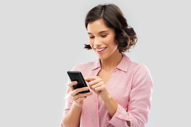 молодая женщина в полосатой рубашке с помощью смартфона - Фото, изображение