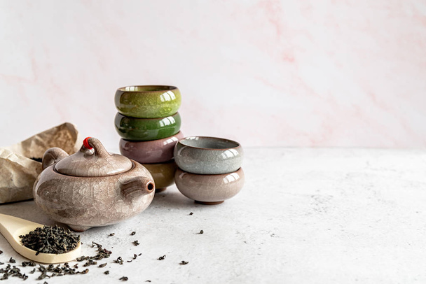 Bule asiático com uma pilha de xícaras de chá coloridas e pacote de chá no fundo de mármore branco
 - Foto, Imagem