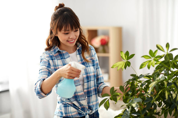 happy asian woman spraying houseplant at home - 写真・画像