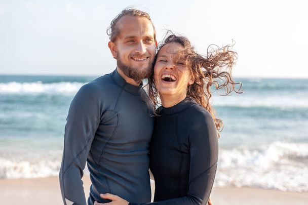 Pareja joven de surfistas sonrientes felices en la costa del océano, concepto de viaje de vacaciones deportivas
 - Foto, Imagen