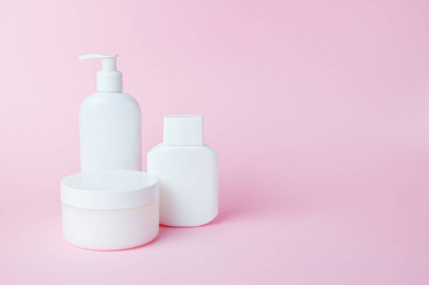 Witte potten cosmetica op een roze achtergrond. Badaccessoires. Gezichts- en lichaamsverzorging - Foto, afbeelding