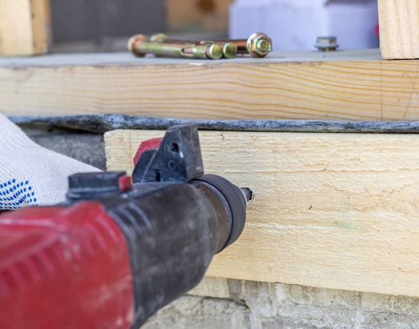 Work drill. Construction of wooden houses. Men's hands in construction gloves. - Foto, imagen