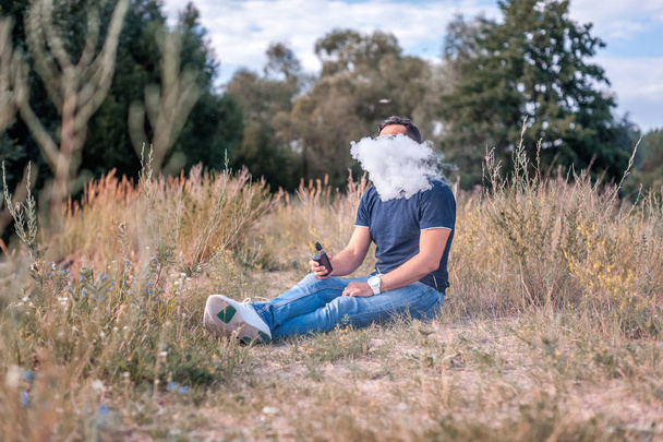 A modern ember pihen a természetben és a pára és bérbeadása le gőz elektronikus cigaretta. Gőzös tevékenység. - Fotó, kép