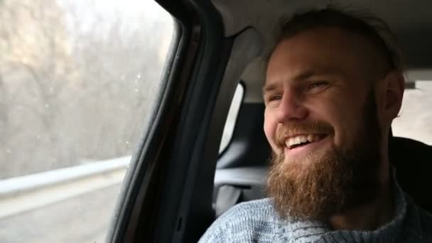 Close-up portrait of a laughing bearded hipster male sitting in a car in the backseat and meditating while looking around - Séquence, vidéo