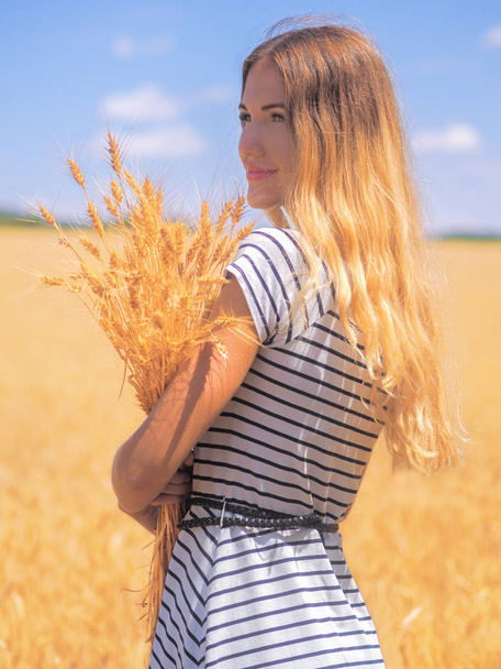 Young woman at the wheat field under the blue sky at the sunny d - Foto, afbeelding