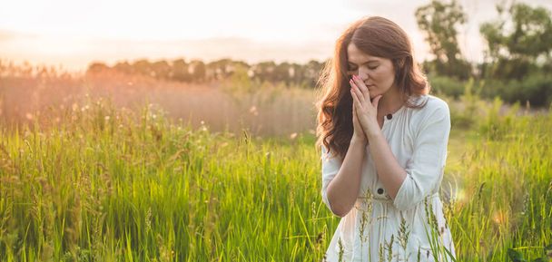 Ragazza chiuse gli occhi, pregando in un campo durante il bel tramonto. Mani giunte nel concetto di preghiera per la fede
 - Foto, immagini