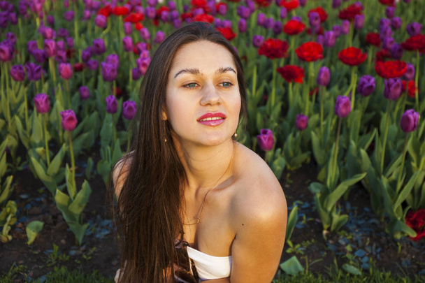 Young brunette women on the background of a glade of tulips flow - Fotoğraf, Görsel
