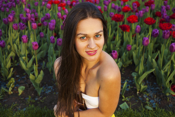 Young brunette women on the background of a glade of tulips flow - 写真・画像