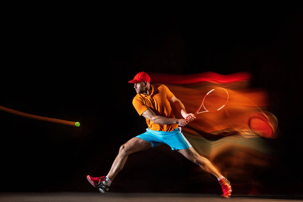 One caucasian man playing tennis on black background - Photo, Image