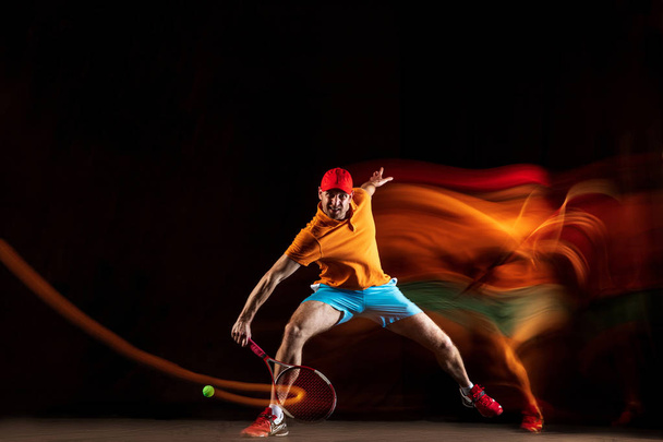 One caucasian man playing tennis on black background - Foto, afbeelding