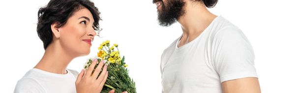 panoramic shot of cheerful latin man giving flowers to attractive woman isolated on white  - Foto, Bild
