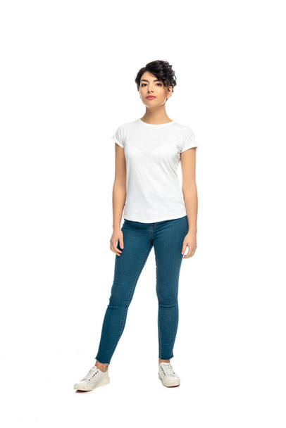 attractive latin brunette woman standing in blue jeans and white t-shirt isolated on white  - 写真・画像