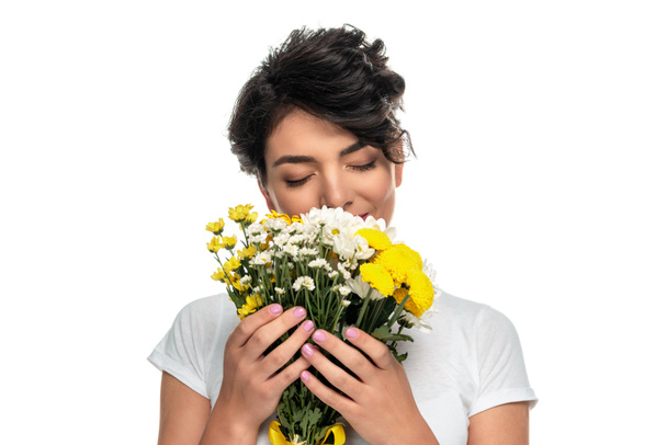 brunette latin woman covering face while smelling flowers isolated on white  - Zdjęcie, obraz