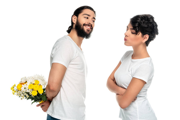 allegro uomo latino che tiene fiori gialli vicino alla donna in piedi con le braccia incrociate isolato su bianco
  - Foto, immagini