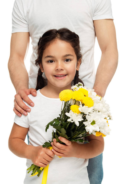 白に隔離された黄色い花を持つラテンの娘の近くに立っている父親のトリミングされた眺め  - 写真・画像