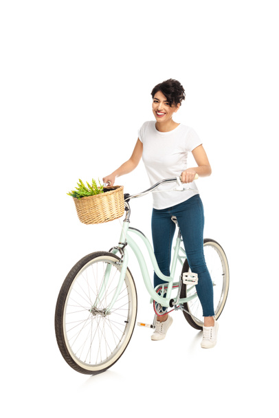 cheerful latin woman riding bicycle and smiling isolated on white  - Фото, зображення