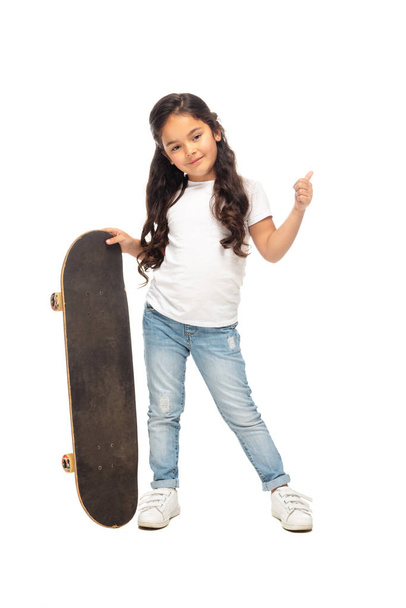 schattig Latin Kid tonen duim omhoog terwijl het houden van Penny Board geïsoleerd op wit  - Foto, afbeelding