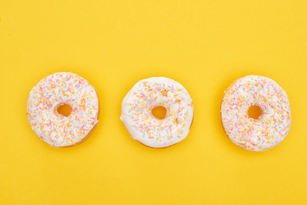 top view of tasty glazed doughnuts with sprinkles on bright yellow background - Φωτογραφία, εικόνα