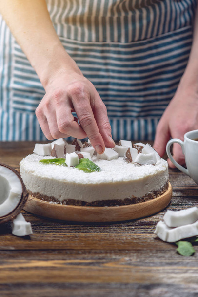Confectioner decorates coconut raw cake with white pulp and mint. Healthy vegan dessert. Gluten and sugar free food - Foto, Bild