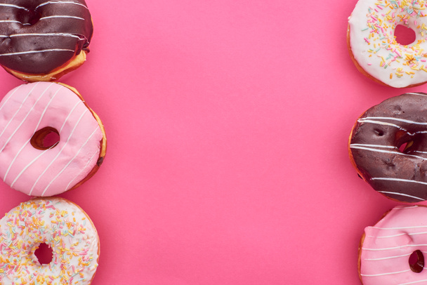 Top uitzicht op de heerlijke geglazuurde donuts op Felroze achtergrond - Foto, afbeelding